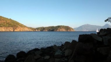 Beyaz yatlar arka planda yelken açıyor ve kıyı şeridinde dağlar..