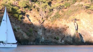 Sahildeki deniz ve dağların arka planında beyaz bir yat var..