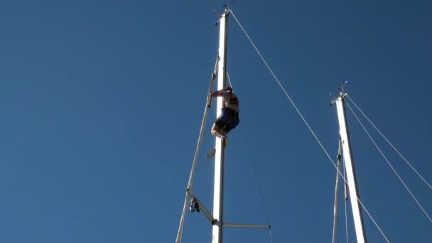 Man op mast van een zeiljacht op achtergrond van helderblauwe lucht. — Stockvideo