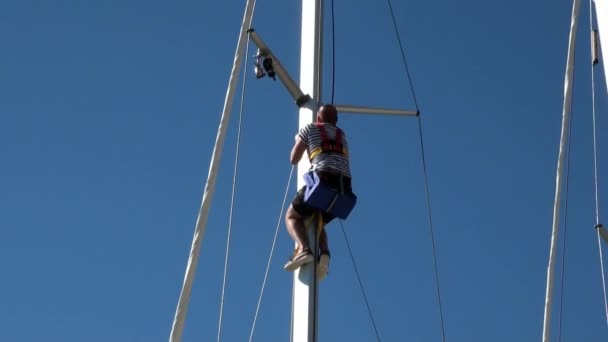 Muž vyleze na stěžeň plachetnice na pozadí jasné modré oblohy. — Stock video