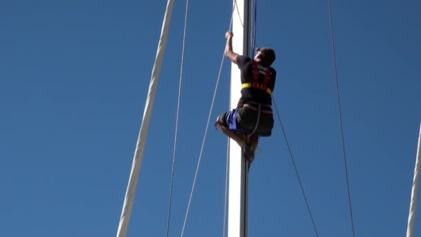 Man op mast van een zeiljacht op achtergrond van helderblauwe lucht. — Stockvideo