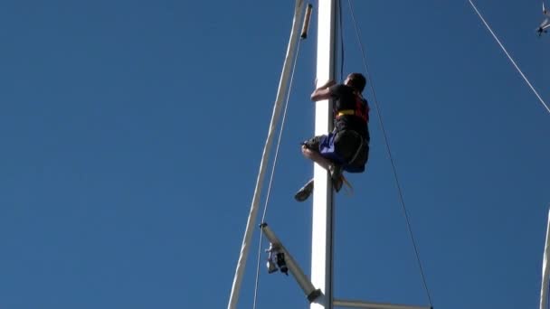 Muž na stožáru plachetnice na pozadí jasné modré oblohy. — Stock video