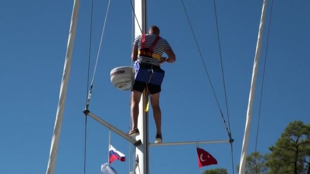 El hombre sube al mástil de un yate de vela en el fondo del cielo azul claro. — Vídeos de Stock