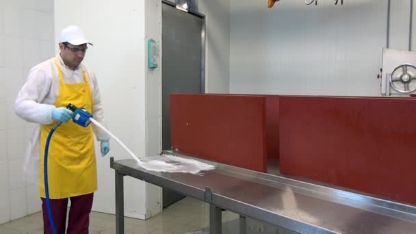 Homem trabalhador lava e desinfecta mesa para cortar carne em oficina industrial. — Vídeo de Stock