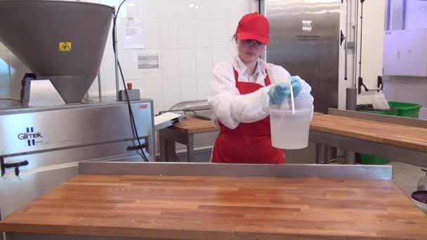 Vrouwelijke werkster in rood schort en pet desinfecteert houten tafel in industriële werkplaats. — Stockvideo