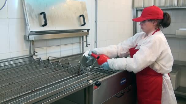 Женщина в красном фартуке и колпаке стирает промышленный фритюрницу в мастерской. — стоковое видео