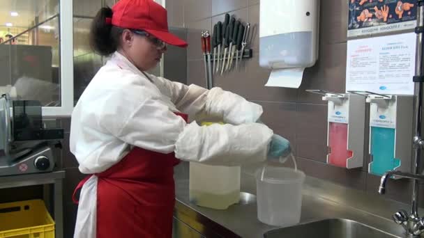 身穿红围裙、头戴帽子的妇女将水倒入容器消毒剂溶液中. — 图库视频影像