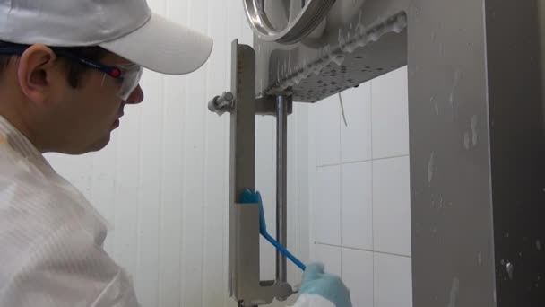 Pracownik myje i dezynfekuje urządzenia do cięcia mięsa w warsztacie przemysłowym. — Wideo stockowe