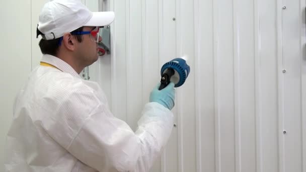 Man werknemer wast en desinfecteert witte muur in industriële werkplaats. — Stockvideo