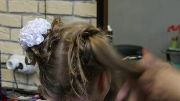 Skapa en frisyr från flätor för ung flicka i frisör. — Stockvideo