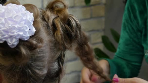 Proces wypełniania warkoczy z białymi kokardkami na głowie młodej dziewczyny w warsztacie fryzjerskim zbliżenie. — Wideo stockowe