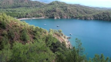 Beyaz yatlar arka planda yelken açıyor ve kıyı şeridinde dağlar..