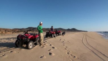 Dörtlü bisiklete binen bir grup turist kum üzerinde ATV 'ye biniyor ve el sallıyor..