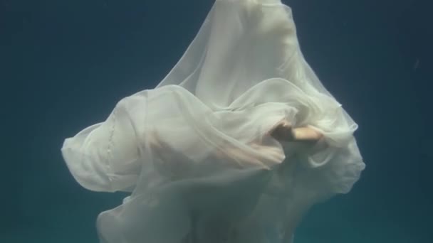 Young woman underwater model in white cloth on background of blue water. — Stock Video