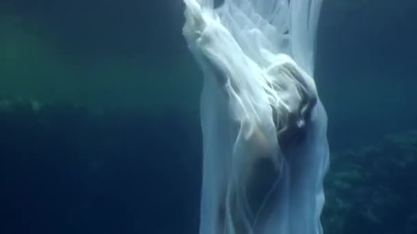 Ung kvinna undervattensmodell i vit duk på bakgrund av blått vatten. — Stockvideo
