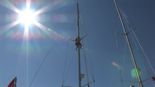 Člověk sedí na stožáru jachty na pozadí modré oblohy a slunce . — Stock video