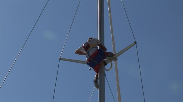 Man sitter på masten av yacht på bakgrunden av blå himmel och sol . — Stockvideo