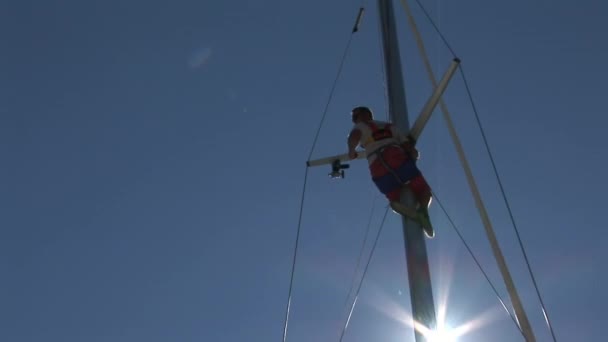 El hombre se sienta en el mástil de yate en el fondo del cielo azul y el sol . — Vídeos de Stock