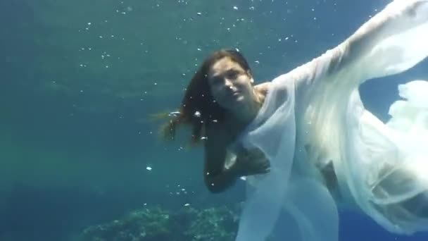 Young woman underwater model in white cloth on background of blue water. — Stock Video