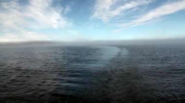 Karanlık gökyüzünün arka planında su yüzeyinde dalgalar ve gün batımında gri bulutlar.