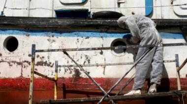 İşçiler tersanede tamirat sürecinde metali boyayla parçalıyorlar..