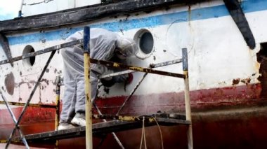 İşçiler tersanede tamirat sürecinde metali boyayla parçalıyorlar..