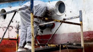 İşçiler tersanede tamirat sürecinde metali boyayla parçalıyorlar..