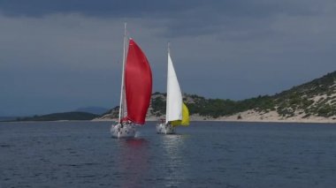 Yunanistan 'daki deniz dalgalarının arka planında kırmızı ve sarı yelkenli iki beyaz yat.