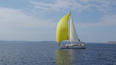 Yunanistan 'da denizin arka planında sarı yelkenli beyaz tekne.