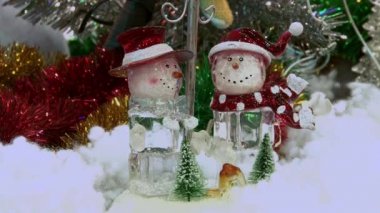 Ağacın altındaki karda komik oyuncak kardan adam. Parıldayan ışıklar arasında Noel ağacında Noel ve Yılbaşı oyuncakları.
