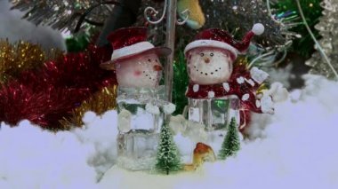 Ağacın altındaki karda komik oyuncak kardan adam. Parıldayan ışıklar arasında Noel ağacında Noel ve Yılbaşı oyuncakları.
