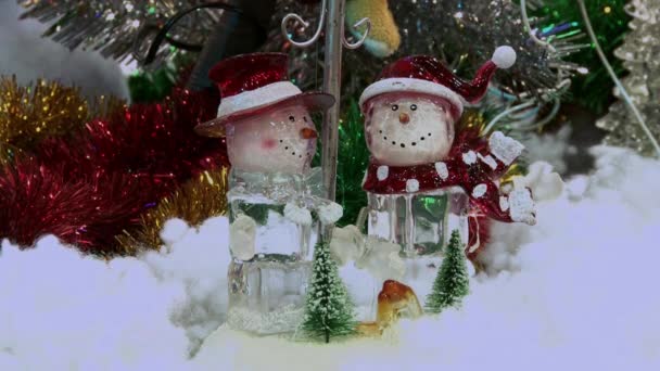 Boneco de neve de brinquedo engraçado na neve debaixo da árvore. Brinquedos de Natal e Ano Novo na árvore de Natal entre as luzes cintilantes . — Vídeo de Stock