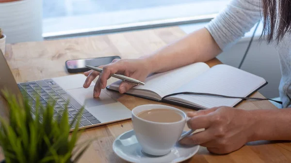 オフィスのノートパソコンで働く女性 机の上のコーヒーカップ ノートパッド ラップトップで閉じます ペンを持って — ストック写真