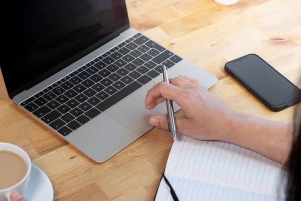 ノートパソコンを使ってペンを持っている女性 オフィスで働く スマートフォンと木製の机 ノートパッドとコーヒー — ストック写真
