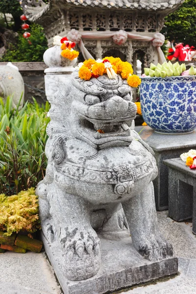 Kinesiska lejon sten staty med ringblommor kransar på huvud — Stockfoto