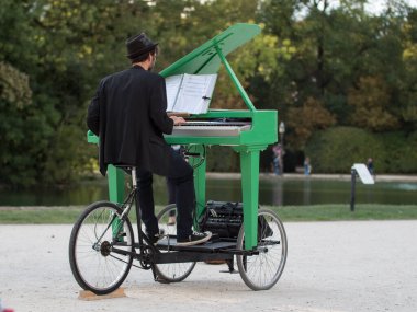 Halk parkında Yeşil Mobil Piyano çalan Şapkalı Piyanist.