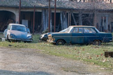 Eskimiş ve paslı arabalar arka planda bir tarla ve yıkılan bir depoda terk edildi..