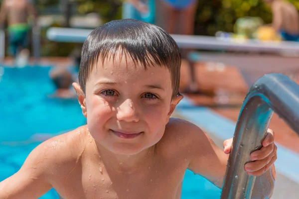 A smiling young boy (5-6) on the ladder of a swimming pool. — Stock Photo, Image