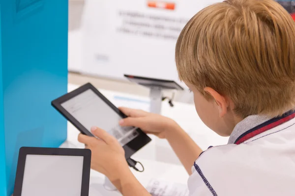 Kid (7-8 jaar) speelt met de tablet pc in een winkel — Stockfoto