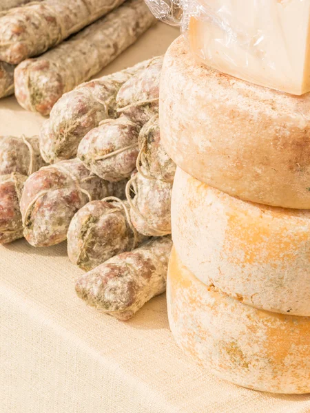 Stacked rounded cheese and group of salami on tablecloth — Stock Photo, Image