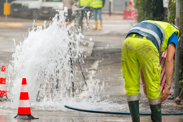 Estrada jorrar água ao lado de cones de tráfego e reparador — Fotografia de Stock