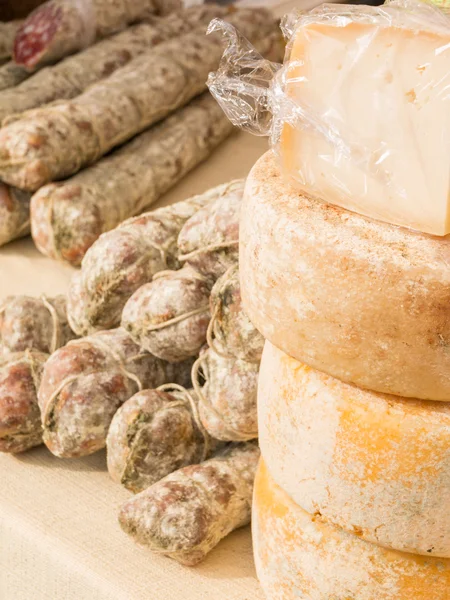 Stacked rounded cheese and group of salami on tablecloth — Stock Photo, Image