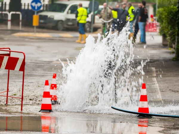 Água de jorro de estrada ao lado de cones de tráfego — Fotografia de Stock