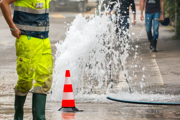 Road spurt water beside traffic cones and a technician — Stock Photo, Image