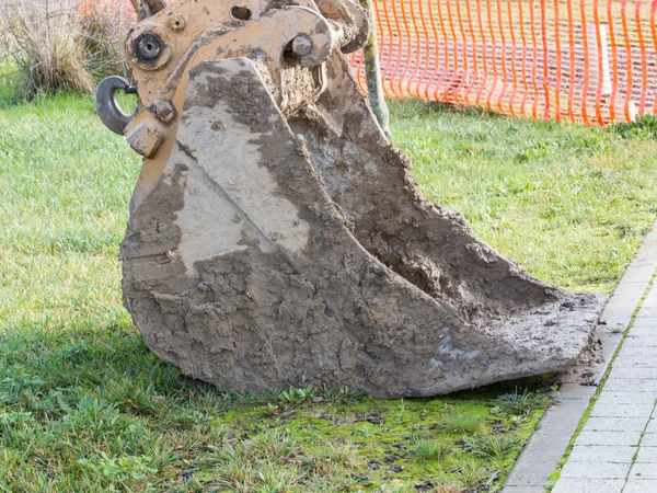 Närbild av leriga grävmaskin spade på gräs nära konstruktion är — Stockfoto