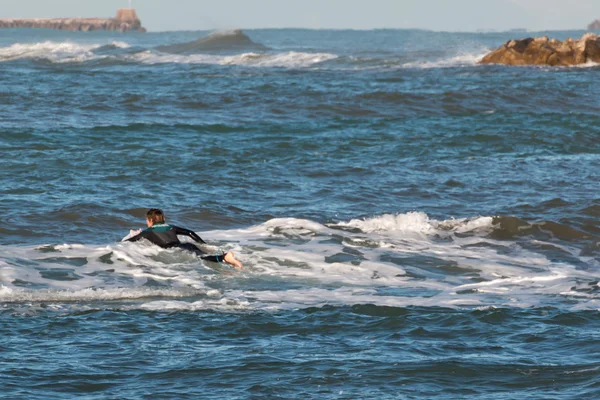 Surfista roupa de mergulho preto que coloca em uma placa no mar entre a onda — Fotografia de Stock