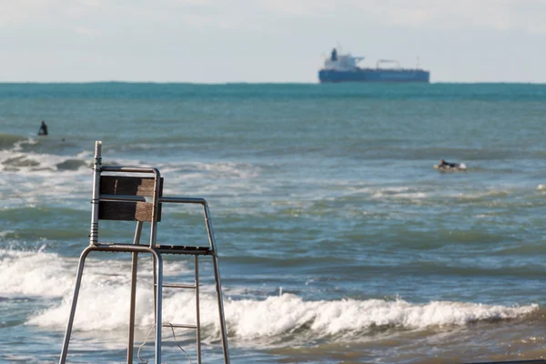 Empty lifeguard chair, surfers in sea and cargo ship in backgrou — Stock Photo, Image