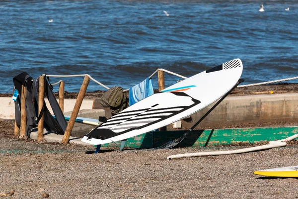 Tabla de surf en blanco y negro en la cuerda cerca de trajes de neopreno — Foto de Stock