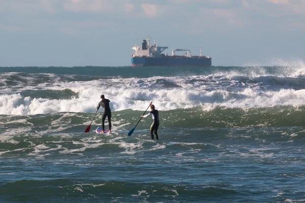 Männer paddeln an Bord in den Wellen, Versorgungsschiff im Hintergrund — Stockfoto