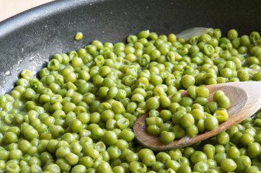 tahta kaşıkla siyah tavada yeşil bezelye yemek